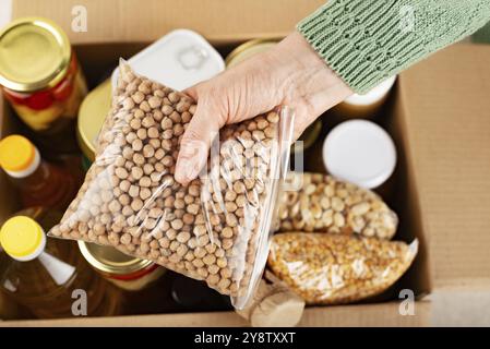 Plastic container with chickpeas in female hand on emergency food box background Stock Photo