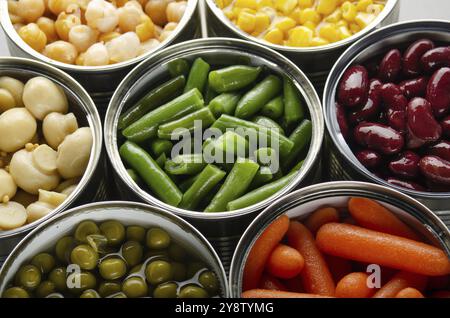 Canned vegetables in opened tin cans on kitchen table. Non-perishable long shelf life foods background Stock Photo