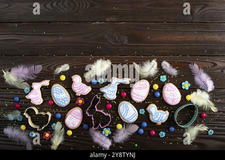 Cookie cutters feathers and Easter frosted cookies in shape of egg, chicken and rabbit on dark wooden background. Flat lay with copy space Stock Photo