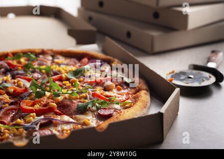 Large Pizza in open carton box and cutter on kitchen table closeup view Stock Photo
