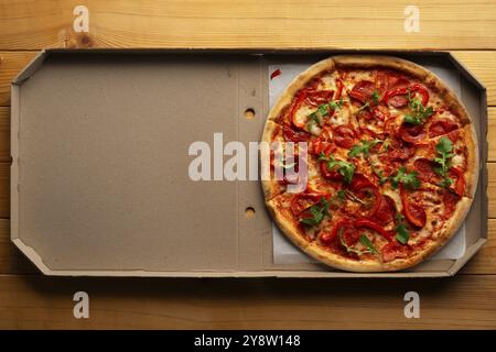 Pepperoni pizza with bell peppers and arugula in open carton box on natural wooden kitchen table flat lay with copy-space Stock Photo