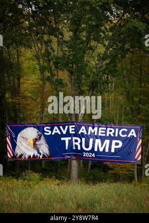 Tyngsborough (also spelled Tyngsboro), MA, USA. Large Pro-Trump 2024 sign hung on the right side of the Northbound lanes of Interstate 95 (I-95), before the 5 November 2024 U.S. Presidential election.  The sign on vacant forested land is along I-95 near the Massachusetts New Hampshire border close to Tyngsborough.  The large sign, about the size of a shipping container, 40 ft (12.2 meters) by 8.5 ft (2.60 meters), is suspended by cable over trees about 200 feet (60 meters) from the Interstate. Stock Photo