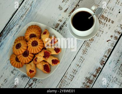 Kurabye, shortbread cookies with thick jam on a white plate and a cup of black coffee on a light wooden table. Top view, flat lay. Stock Photo