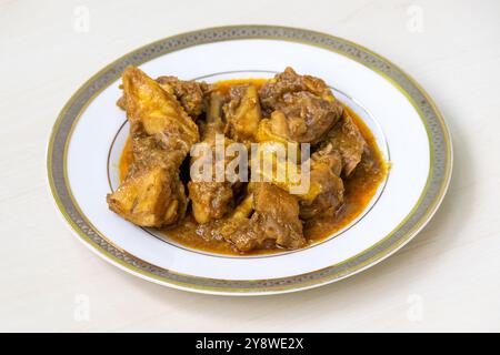 Delicious homemade chicken curry or chicken bhuna on a white plate, placed on light wooden surface. Authentic Bengali cuisine cooked deshi chicken mea Stock Photo