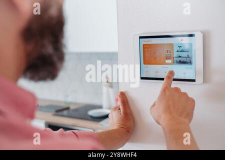 Man using smart thermostat, adjusting, lowering heating temperature at home. Concept of sustainable, efficient, and smart technology in home heating Stock Photo