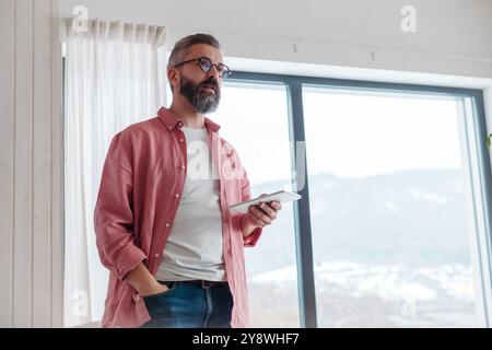 Man using smart thermostat, adjusting, lowering heating temperature at home. Smart home controlling roller blinds. Stock Photo