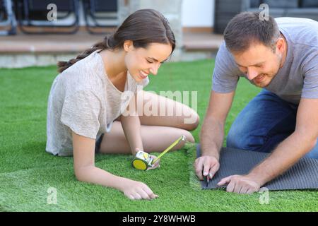 Happy couple installing artificial turf in the garden at home Stock Photo