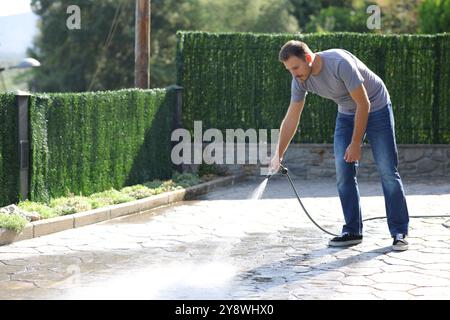 Man washing garden floor using hose at home Stock Photo