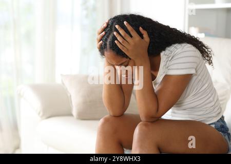 Sad black woman complaining alone sitting on a couch at home Stock Photo