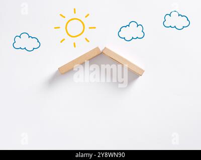 Home insurance, ownership or real estate investment concept. Wooden blocks creating a roof with sun and clouds drawn in the background over a white su Stock Photo