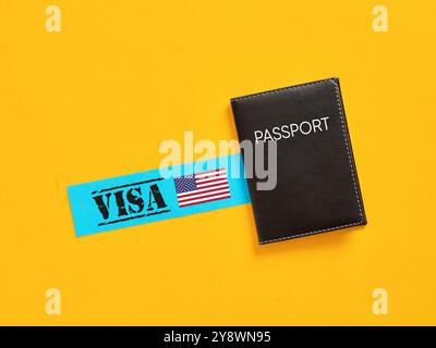 Applying for USA visa. Black passport is lying near blue paper with American visa and usa flag on yellow background. Stock Photo