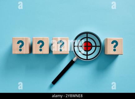 Clarifying and setting business goals and objectives. Goal analysis. Magnifying glass focusing on target inside question marks on wooden cubes over bl Stock Photo