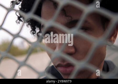 teen with curly hair behind metal chain link fence Stock Photo