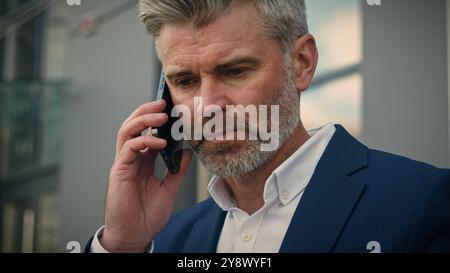 Caucasian old retired business man mature senior businessman leader employer talking mobile smartphone put on glasses end finish call putting phone in Stock Photo