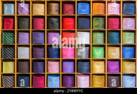 Showcase with multicolored ties. View of different colors ties in showcase. Multicolored man. Showcase of rolled neckties at store. Coiled ties on shelf at shop. Twisted neckties beautifully stacked. Stock Photo