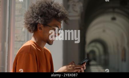 African American ethnic guy male man student using mobile phone in college university high school scrolling smartphone smiling happy e-commerce social Stock Photo