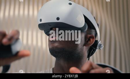 3d world gaming African American man male guy using controllers VR helmet virtual augmented reality glasses high-tech Internet technology futurism Stock Photo