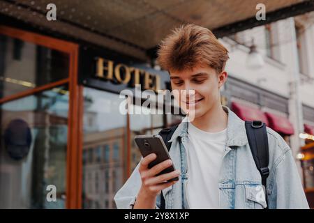 Young man tourist using his smartphone standing outside hotel Stock Photo