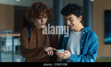 Two teenagers friends Caucasian males men guys pupils students schoolboys walking going in corridor university college school boys looking in mobile Stock Photo
