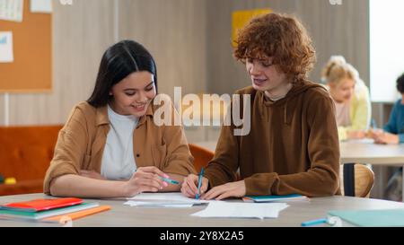 School academy college class lesson couple friends Caucasian girl female schoolgirl boy male guy schoolboy together at table in classroom studying Stock Photo