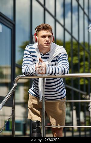 The young man leans against a railing, immersed in music while enjoying the warm sun. Stock Photo