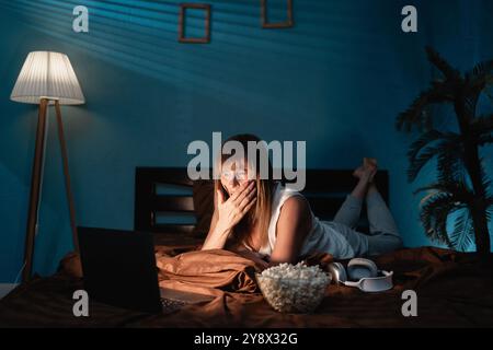 scared mature woman watching horror movie on bed. horror movie concept Stock Photo