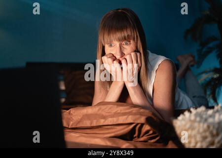 scared mature woman watching horror movie on bed. horror movie concept Stock Photo