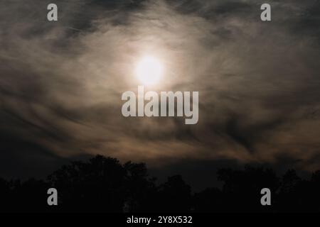 A soft focus image of the sun partially obscured by thick clouds creating misty and atmospheric sky with muted light and a dramatic, moody feel Stock Photo