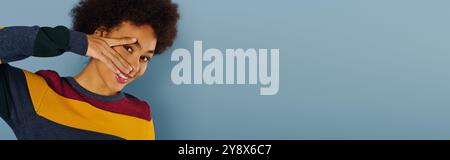 A young woman with curly hair smiles brightly while playfully framing her face with her hands. Stock Photo