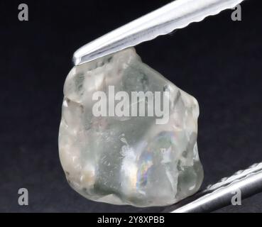 Iridescent Gemstone Captured in Silvery Tongs on Dark Background. Stock Photo