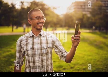 Portrait of cheerful adult man in park who is using smartphone. Stock Photo