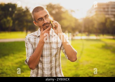 Portrait of worried adult man in park who is talking on phone. Stock Photo