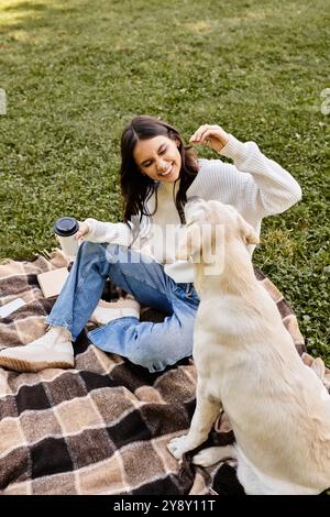 A young woman in warm attire playfully interacts with her dog on a grassy field. Stock Photo