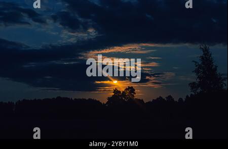 Night sky with a large round moon hiding behind clouds.Bright full moon. Stock Photo