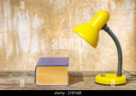 A table lamp and a book on an old wooden table against a shabby background Stock Photo