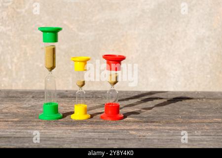 Three hourglasses on rustic weathered wooden table. Time is running Stock Photo