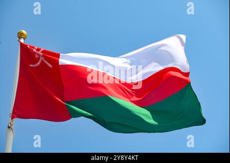 Flag of Oman on flagpole waving against blue sky Stock Photo