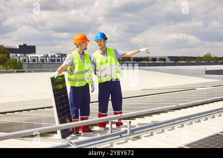 Workers technicians standing on rooftop and installing solar panels for sustainable energy Stock Photo