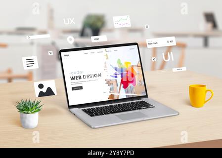 Laptop on a workspace displaying a web design studio webpage, with graphic web modules and elements floating around, illustrating the concept of dynam Stock Photo