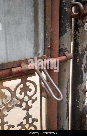 old rusty bolt hinge and lock on metal outdoor gate, corroded sliding locking hardware in soft focus and copy space Stock Photo