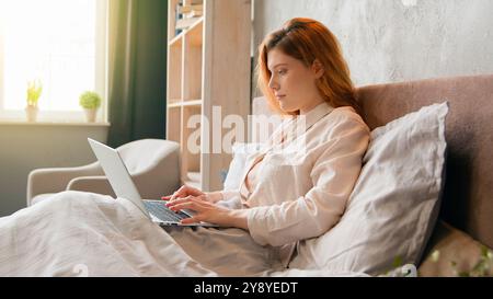 Caucasian woman in tranquil morning freelancer businesswoman student girl in bed after wake up sleeping typing computer laptop working distant from Stock Photo