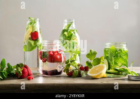 Infused water with strawberries, raspberries, lemon, cucumber and mint in glass jars on wooden table, natural detox drink concept. Stock Photo