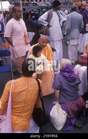 Hindu monk with a child sitting on his knee, and his/ ger parents kneeling in from of the monk.  The festival of Rathayatra, Trafalgar Square London England 2005 2000s UK HOMER SYKES Stock Photo