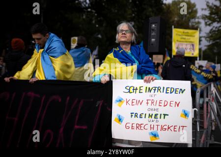 Gegenprotest Friedensdemo DEU, Deutschland, Germany, Berlin, 03.10.2024 Gegenprotest von Mitglieder der Gemeinde aus der Ukraine und ukrainesolidarische Organisation Vitsche mit Plakat Scheinfrieden ist kein Frieden ohne Freiheit und Gerechtigkeit gegen die Russlandfreundliche Demonstration der deutschen Friedensbewegung unter dem Motto Nein zu Kriegen und Hochruestung Die Waffen nieder Ja zu Frieden und soziale Friedenspolitik vor der Siegessaeule in Berlin Deutschland . Der Protest verschiedenen Initiativen und Parteien wie Buendnis Bündnis BSW Sahra Wagenknecht , SPD, Die Linke , Gewerkscha Stock Photo