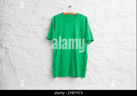 Green teeshirt hanging in front of white painted stone wall Stock Photo