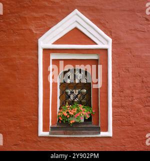 An old style white window with flowers on a red wall. Window ornament in architecture. Stock Photo