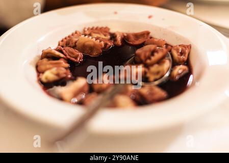 Once upon a time the monks used to confort the pilgrims in the cold winter, serving Ravioli in a plate of warm red wine. Ravioli nel vino. Stock Photo