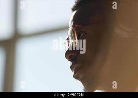 Moody side view close up of African American man wearing glasses and looking at computer screen in sunlight, copy space Stock Photo