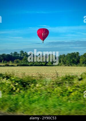 Red hot air balloon, floating low over green field. Stock Photo