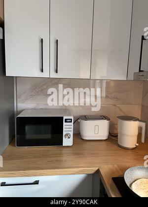 Corner of modern kitchen features white cabinets, gold faucet, and ...